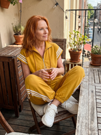 Zip-front stripe-panel jumpsuit for women, mustard yellow with white striped sleeves and cuffs.